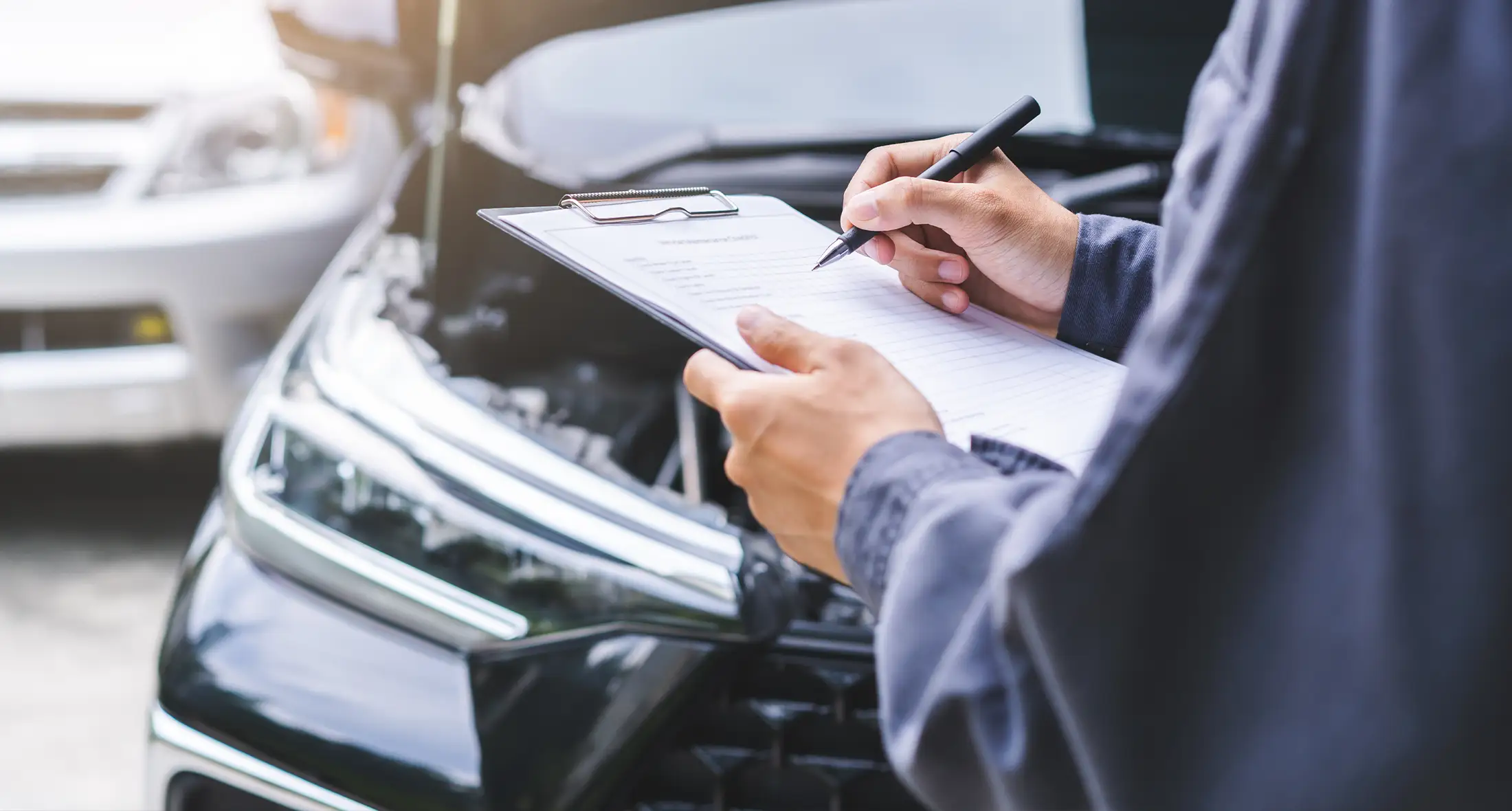 Ein Automechaniker schreibt eine Checkliste auf ein Klemmbrett, während ein anderer den Motor prüft, um einen Kostenvoranschlag für die Reparatur zu erstellen.